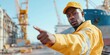 © Tadeusz - Confident Black male worker signaling at a busy dockyard in bright yellow work attire.