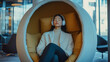 © dK - Woman finding calm in a wellness pod within an open office area