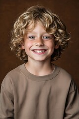 Wall Mural - A young boy with blonde hair is wearing a brown shirt and smiling. He has a bright and cheerful expression on his face, making him appear happy and content