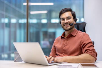 Wall Mural - Professional Hispanic businessman in office environment with headset, typing on laptop, exuding confidence and approachability, perfect for customer service or remote work concepts.