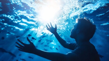 Wall Mural - Silhouette of a man underwater with his arms outstretched towards the surface, reaching for the sunlight, as fish swim around him.