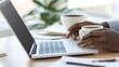 © PSCL RDL - Close-up of a laptop, coffee cup, and notebook on a desk, with hands typing on the keyboard, symbolizing a busy workday