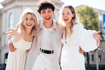 Young three stylish friends posing in the street. Fashion man and two cute female dressed in casual summer clothes. Smiling models having fun. Cheerful women and guy outdoors, in sunny day