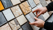 © altitudevisual - Person selecting from various ceramic tile samples with diverse textures and colors in a showroom or home improvement store setting.