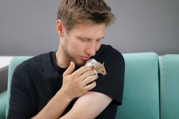 A hamster rests comfortably in the hands of a person seated on a soft couch. The living room is bright and inviting, creating a warm atmosphere for relaxation and bonding