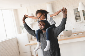 african happy father playing games and having fun with little small preteen daughter, sitting piggyb