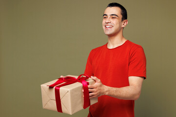 Side view young middle eastern man wear red t-shirt casual clothes hold present box with gift ribbon bow look aside on area isolated on plain pastel green background studio portrait Lifestyle concept