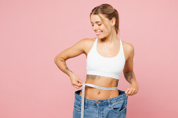 Poster - Young woman she wear white top casual clothes hold measuring tape on waist show loose pants isolated on plain pastel light pink background. Proper nutrition healthy fast food unhealthy choice concept.