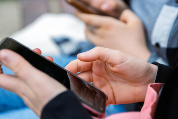 Wall Mural - Closeup of young people hands holding mobile phones. Two teenager girls are using their smartphones outdoors, texting or browsing. Selective focus. Copy space