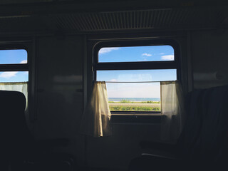 atmospheric photo from a train that goes along the seashore, view from the window with white curtains, travel and trip concept