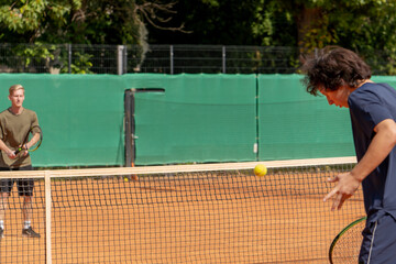 professional tennis court young curly guy playing tennis with blond opponent pair training active rest practicing serve with racket