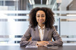 © Tetiana - Portrait of a young African American woman in a suit and headset sitting in the office at a desk, looking and smiling at the camera