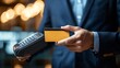 © Ilja - Close-up of Businessman Using Credit Card for Contactless Payment, Focus on Terminal.