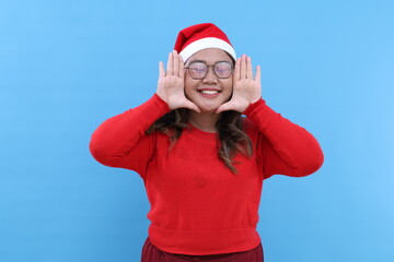 Asian woman smiles broadly keeps palms near rouge face expresses positive emotions wears red turtleneck awaits for holiday event poses against blue background