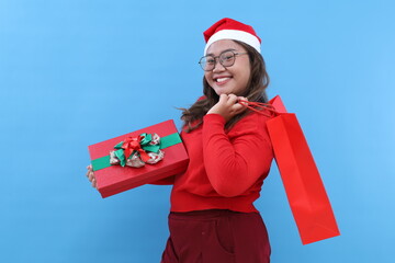 Young beautiful cheerful Asian woman posing with holiday presents isolated over blue background. Christmas shopping. Concept of youth culture, emotions, facial expression, fashion