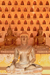 Wall Mural - Three big buddha statues in front of a wall filled with many miniature buddha figurines in the cloister wall of Wat Si Saket, a buddhist temple in Vientiane, Laos