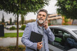 © Miljan Živković - senior man talk on mobile phone and hold clipboard in the parking lot