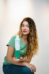 Young woman with curly hair in casual attire holding a bottle of skincare product