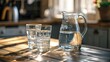 © Lasvu - Water-filled glass and jug on wooden kitchen table