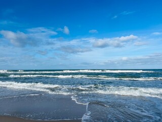 Wall Mural - Blue sea horizon, blue sky with some white clouds, waved seashore, natural blue color 