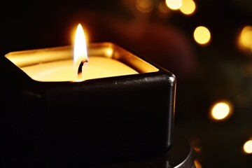 Wall Mural - A close-up of a lit candle in a black holder with a warm flame and blurred background lights, evoking a cozy and festive atmosphere. The bokeh effect adds depth and warmth to the image