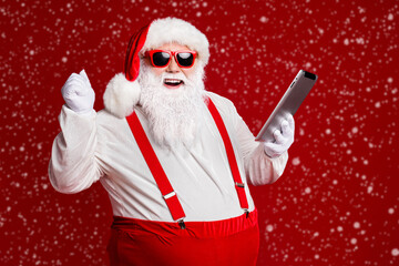 Portrait of his he attractive cheerful cheery lucky fat white-haired Santa using gadget ebook having fun fast speed isolated bright vivid shine vibrant red burgundy maroon color background