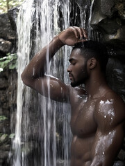 Muscular man standing under a waterfall with eyes closed