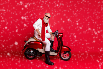 Wall Mural - Fancy grandfather santa man posing sitting on vintage moped wear jumper and trousers isolated red background