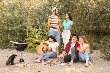 Wall Mural - Young woman playing guitar with her friends on beach at barbeque party