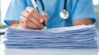 © Rossarin - A healthcare professional in scrubs writes notes on a stack of documents, emphasizing the importance of paperwork in medical practice.