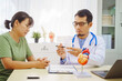 © NanSan - A doctor man sits at a desk in a hospital, explaining heart disease symptoms to a female patient. They discuss chest pain, palpitations, fatigue, dizziness, and the risks of myocardial ischemia