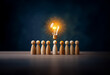 © joeycheung - A glowing light bulb hovers above a row of wooden figures, symbolizing inspiration and innovation within a team.