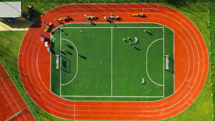 Aerial view of a vibrant sports field and running track. An overhead aerial view of a green sports field with soccer goals and various equipment, surrounded by a bright red running track.