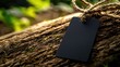 © Vodkaz - Blank black tag tied to tree trunk in natural setting, with green foliage blurred behind.