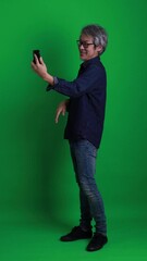 Wall Mural - A vertical shot of a senior Asian man standing against a green background.