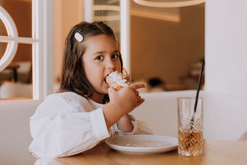 A little girl eats a big flat croissant in a cafe