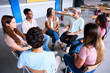 © CarlosBarquero - Diverse happy group of high school students sitting on chairs in circle interacting during lesson. Multiracial adolescents talking together to their classmates and female teacher in support class