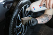 © alones - Professional man applying tire blackening agent to brush in detailing service. Car wash and wheel care