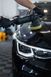 © alones - Professional man with polishing tool polishing black car in garage . Detailing. Varnish care and scratch removal