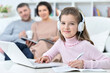 © aletia2011 - Cheerful little girl using a laptop at home with her parents in the background.