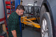 © Alejandro - Mechanic elevating car on hydraulic lift in workshop