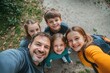 © Tadeusz - Cheerful father and his three children smiling for a selfie outdoors.