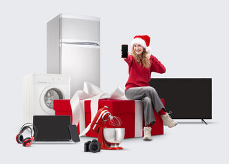 Wall Mural - Electronics and appliance store Christmas shopping, smiling woman showing smartphone and thumbs up sitting on big gift box among household appliances, top offers and sales of Christmas shopping online