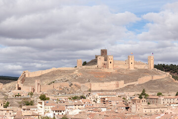 Wall Mural - Majestic medieval castle with fortified walls overlooking a historic village under a cloudy sky