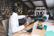 © BullRun - African American man in headphones pointing toward someone off-screen while working on a laptop in a cozy home setting. Background features a festive Christmas tree and holiday lights