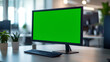 © Thanakorn - A modern computer monitor with a bright green screen sits on a desk, surrounded by a plant and a sleek keyboard in a well-lit office environment.