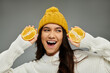 © Bliss - A joyful young woman sports a yellow beanie, holding fresh orange halves and smiling brightly.