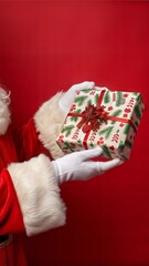 Image of hand of santa claus holding christmas gift with copy space on red background. Christmas, tradition and celebration concept.