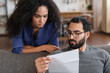 © InsideCreativeHouse - Budget Planning. Stressed thoughtful mixed race couple spouses holding papers and calculating family spends together checking documents, suffering financial crisis, closeup shot