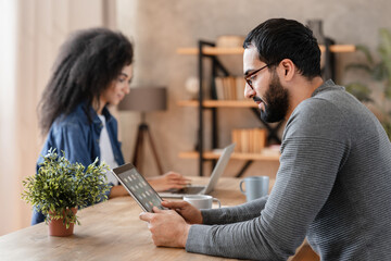 A man and a woman are working at a table at home. Married couple sit at a table in the living room with laptop digital tablet . Arabian guy and African girl work from home